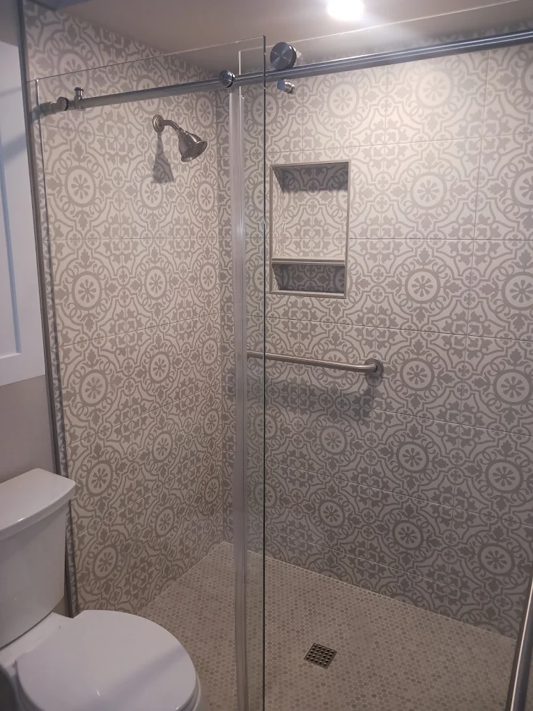 Walk-in shower with patterned gray and white tile, a recessed niche, and a grab bar